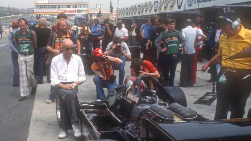 Bald Gunnar Nilsson sits on Lotus wheel of Mario Andretti car in Brands Hatch pitlane 1978
