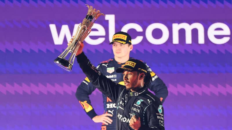 Lewis Hamilton holds up trophy for winning 2021 Saudi Arabian GPas Max Verstappen looks straightfaced behind him