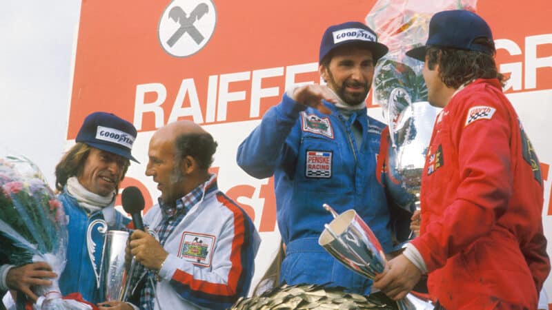 John Watson on the podium after winning the 1976 Austrian GP as Stirling Moss interviews Jacques Laffite