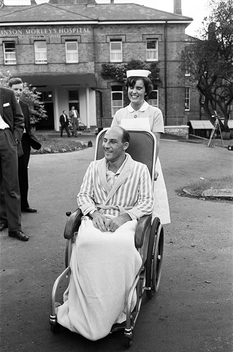 Stirling Moss is pushed by a nurse in wheelchair at Atkinson Morley Hospital in 1962