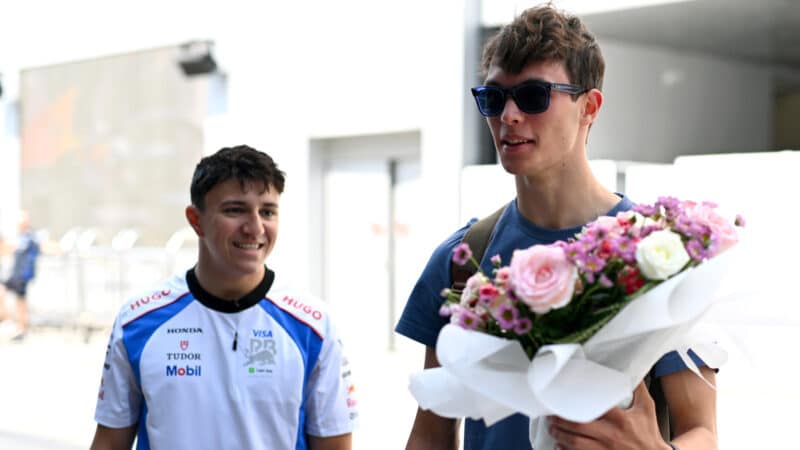 Isack Hadjar looks at Oliver Bearman holding a bunch of flowers in the paddock in Saudi Arabia